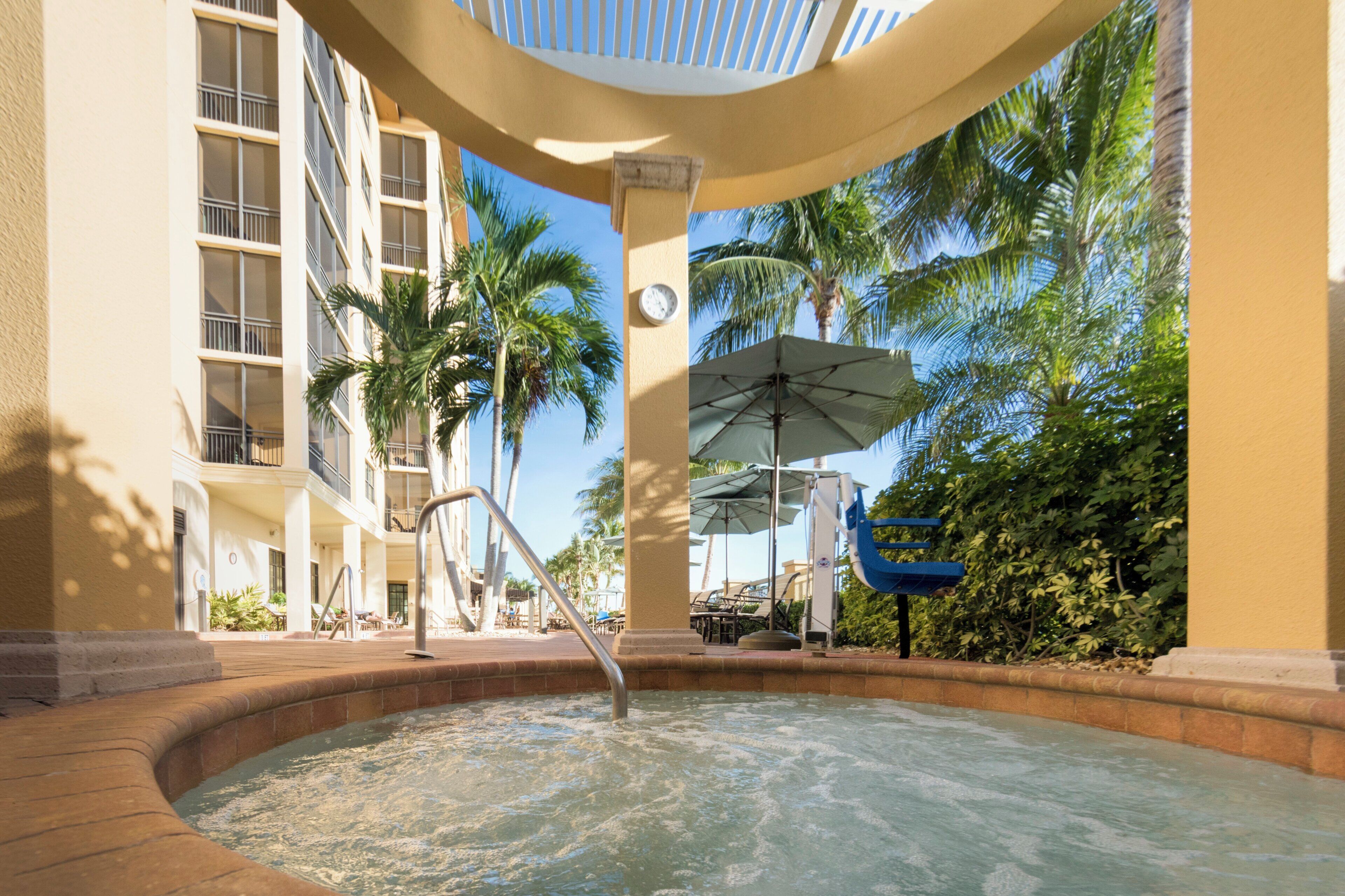 A hot tub area with a pool, palm trees, and a building with balconies.