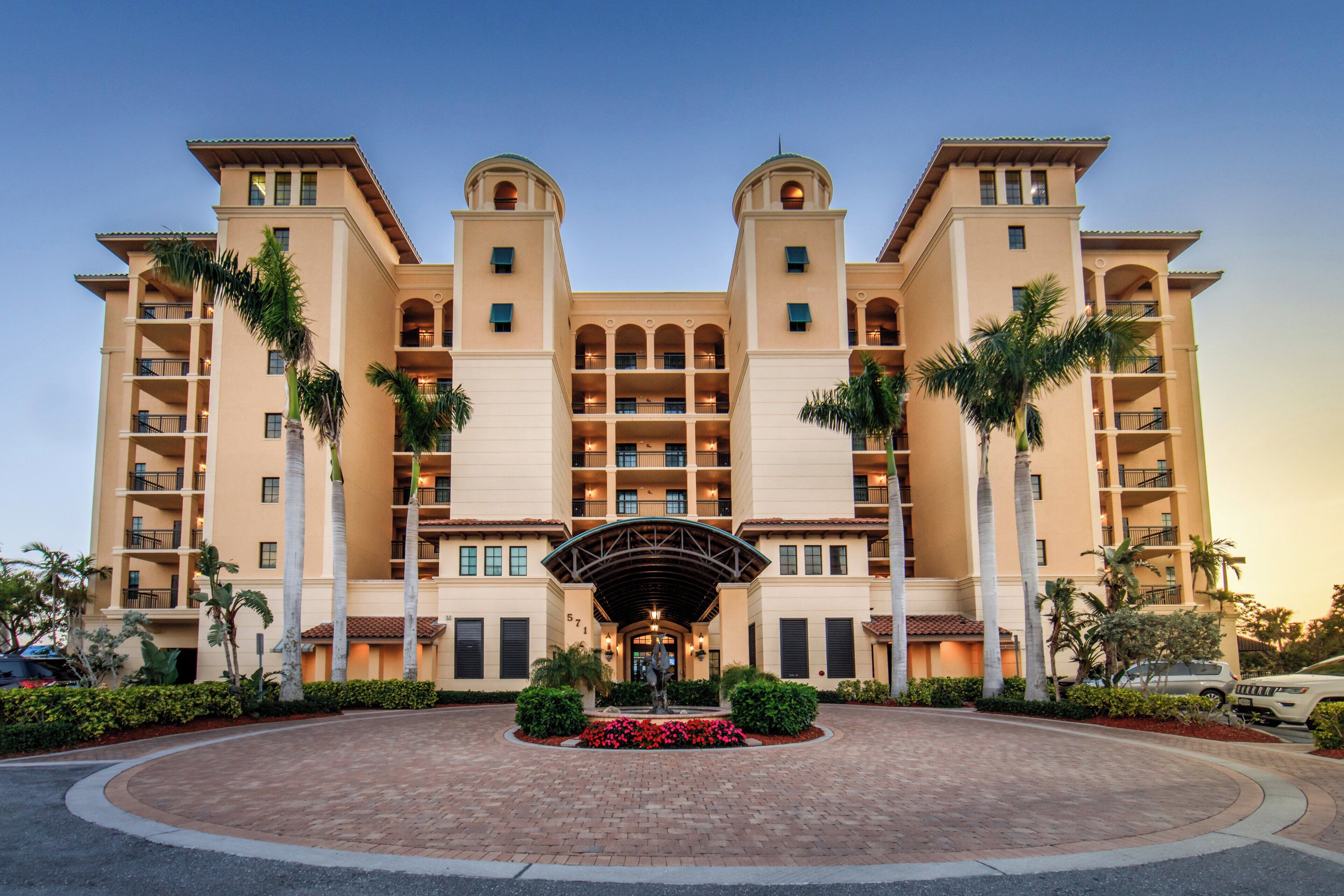 A multi-story hotel with a central courtyard, palm trees, and a fountain.