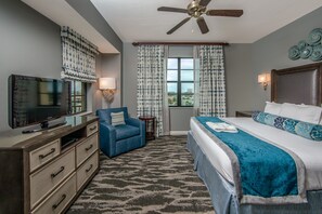 A hotel room with a bed, a television, a desk with drawers, a chair, a ceiling fan, and curtains. - Holiday Inn Club Vacations Sunset Cove Resort by IHG (Marco Island)