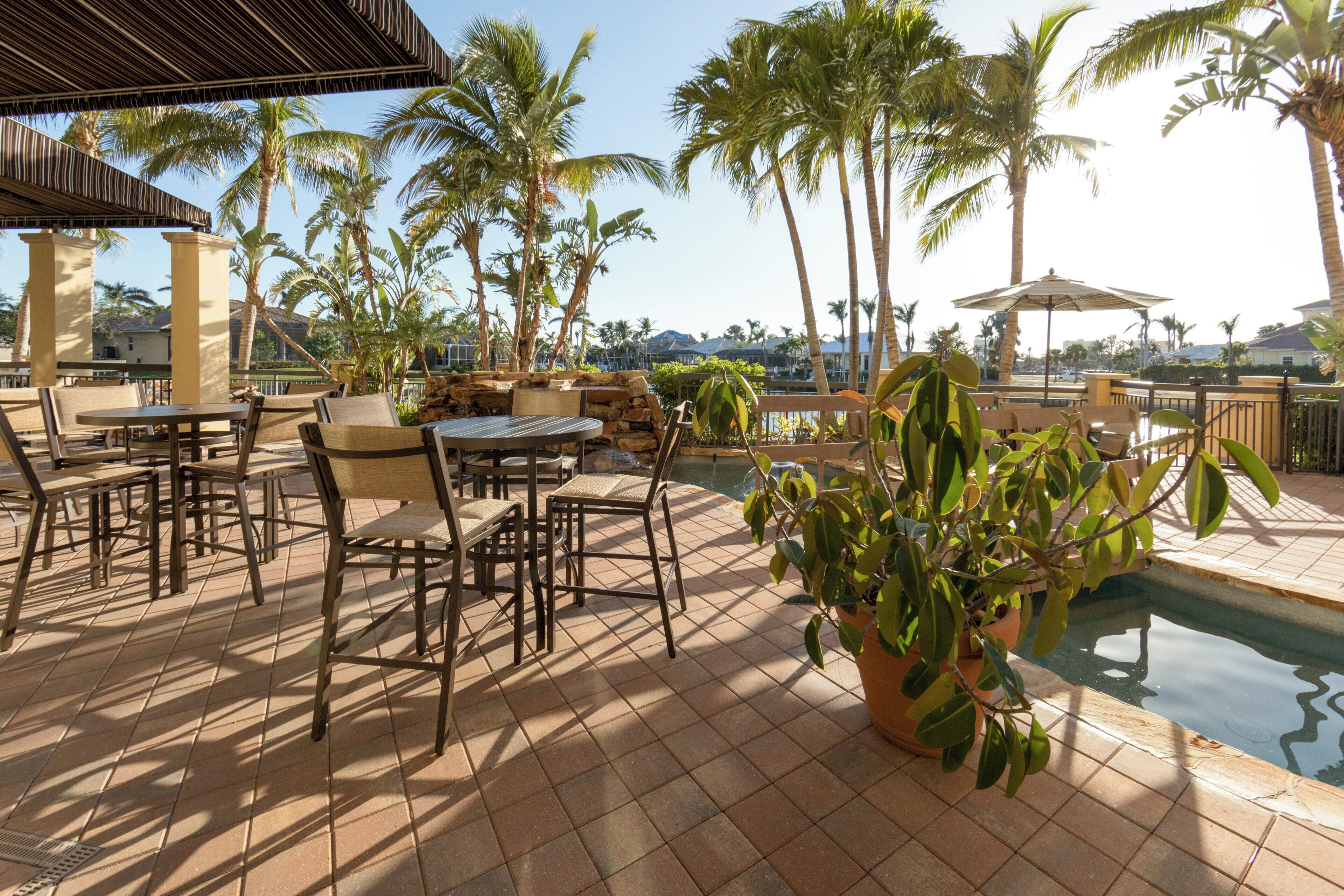 An outdoor patio area with tables and chairs, a pool, and palm trees.