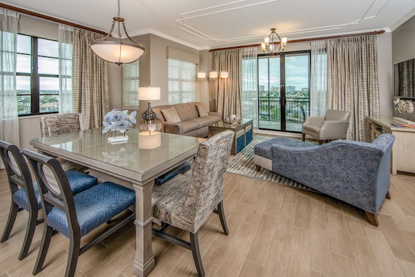 A spacious living area with a large dining table, comfortable seating, and a balcony with a view.