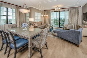 A spacious living area with a dining table, chairs, sofas, and a large window offering a view of the cityscape.