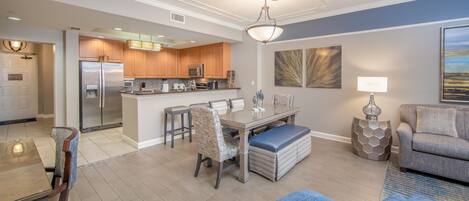 A modern kitchen with stainless steel appliances, a dining area with a glass table, and a living room with a blue sofa.