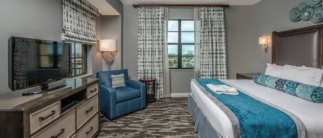 A hotel room with a bed, a television, a desk, a chair, a ceiling fan, and a window with curtains.
