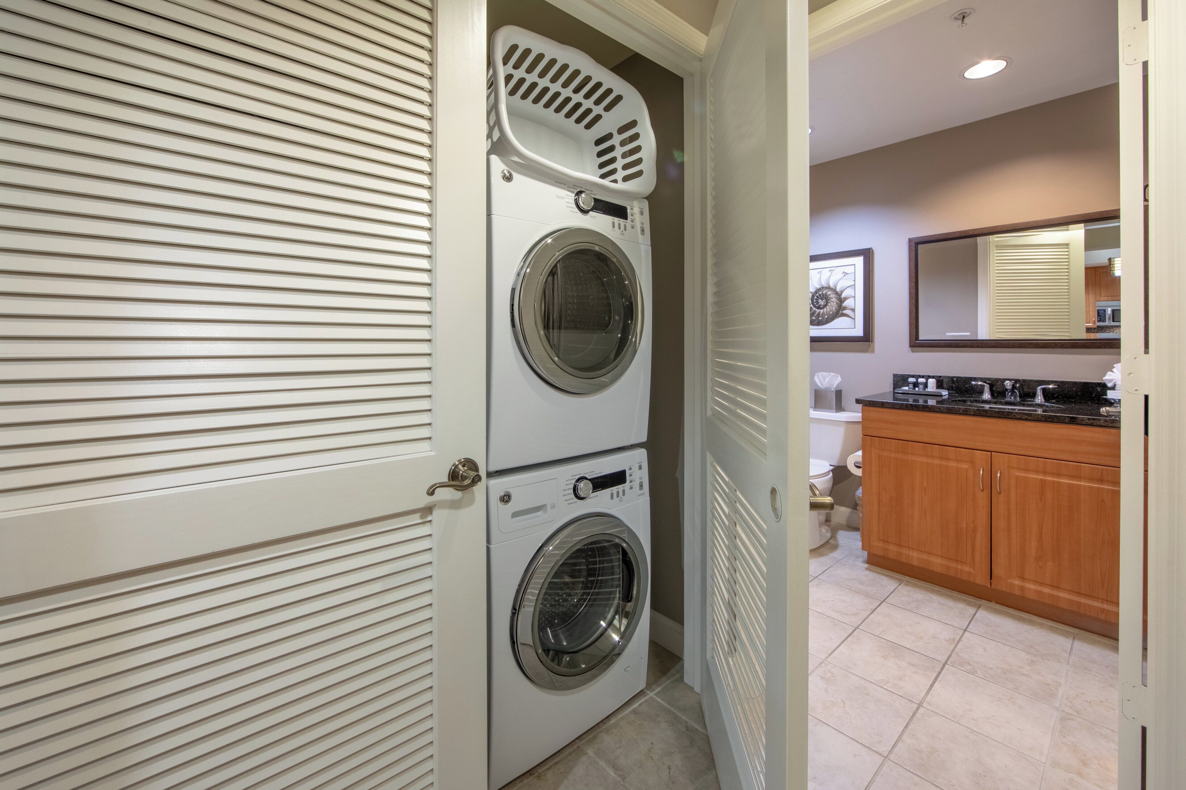 A laundry room with two stacked front-loading washers and dryers, a wooden cabinet, and a mirror above the sink.