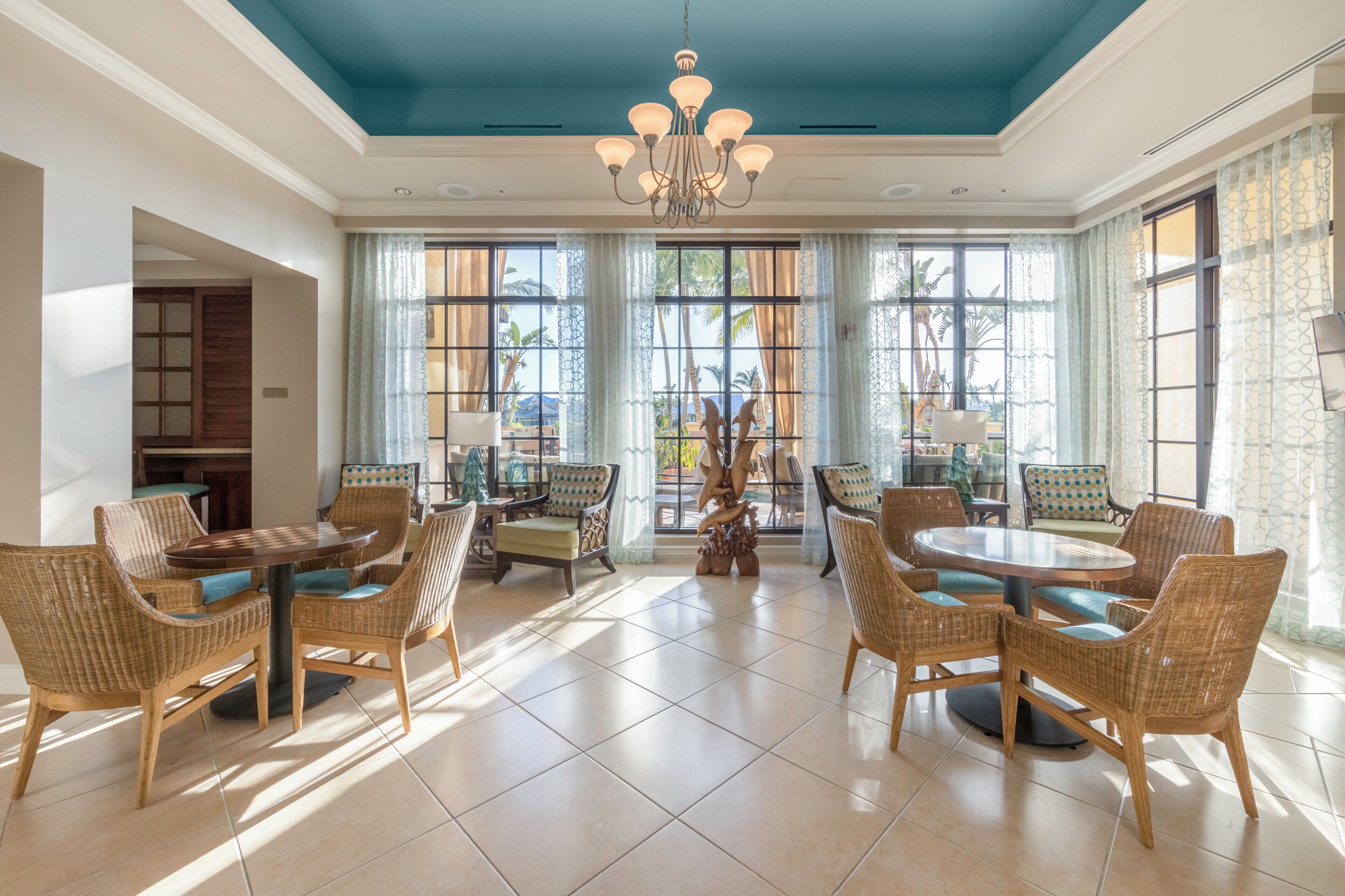 A spacious dining area with wicker furniture, large windows, and a blue ceiling.