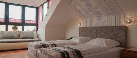 A bedroom with two beds, a sofa, a nightstand, and a wall-mounted light fixture.
