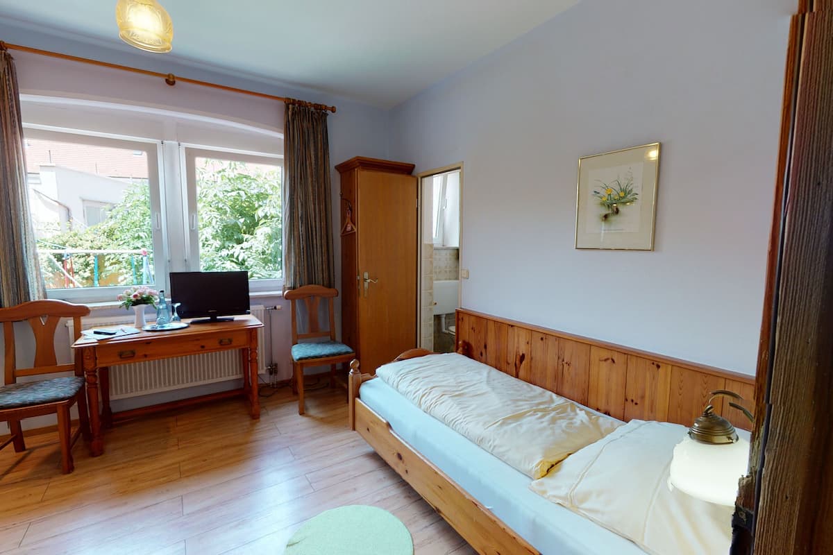 A room with a bed, a desk with a computer, a chair, and a window with curtains.