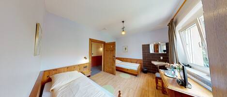A room with two beds, a wooden floor, a small table with a mirror, and a window with curtains.
