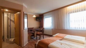 Habitación de hotel con cama, escritorio, silla, televisión y zona de ducha.