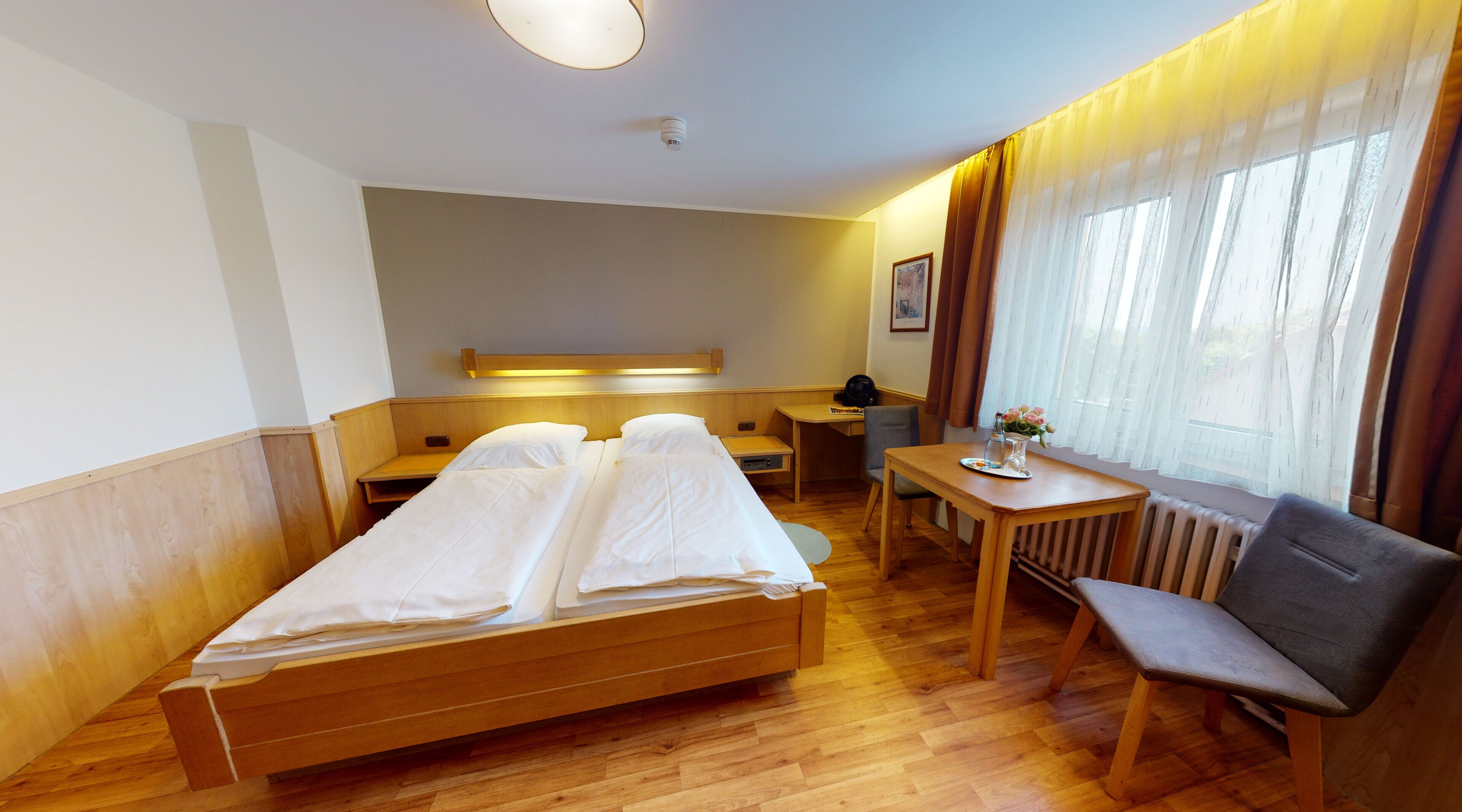 A hotel room with a wooden bed, a desk, a chair, and a radiator.