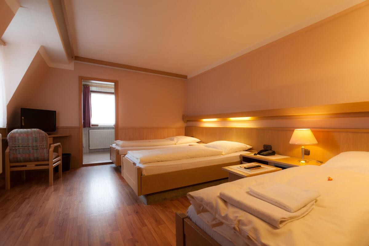 A hotel room with two beds, a desk, a chair, a TV, and a lamp.