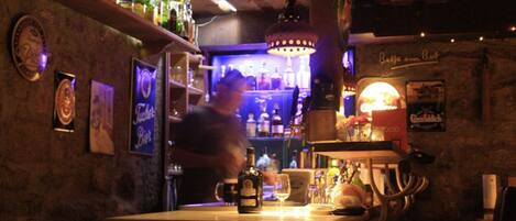 Un espace bar avec un comptoir en bois, des étagères remplies de bouteilles et un luminaire suspendu.