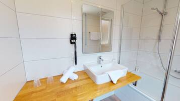 Een moderne badkamer met een houten wastafelmeubel, een witte wastafel, een spiegel, een handdouche en een telefoon.