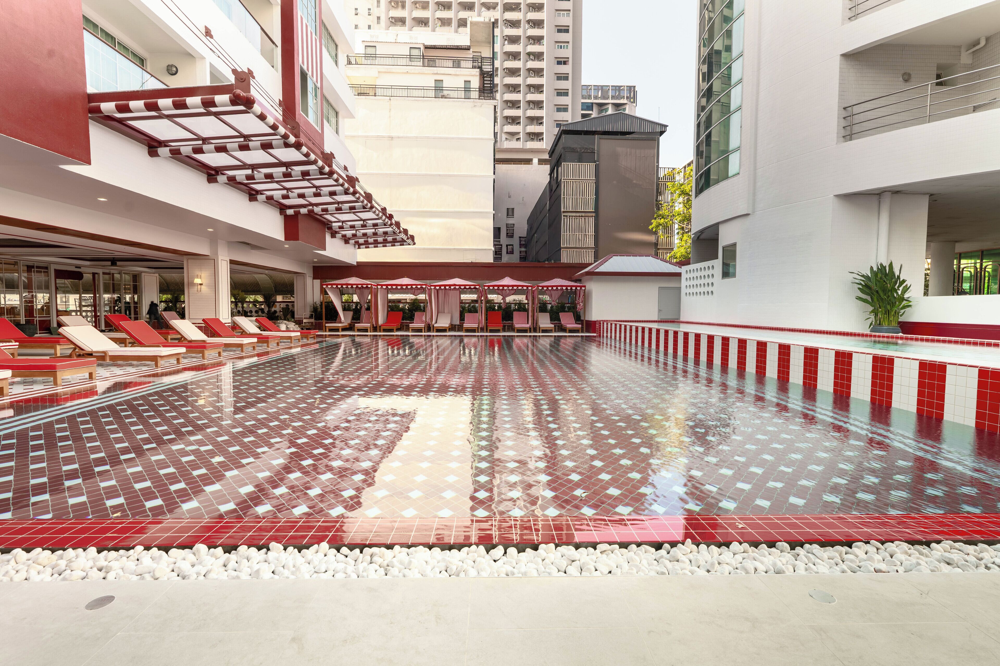 A swimming pool with red and white tiles, lounge chairs, and a covered seating area.