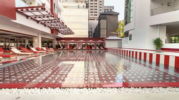 A swimming pool with red and white tiles, lounge chairs, and a covered seating area.