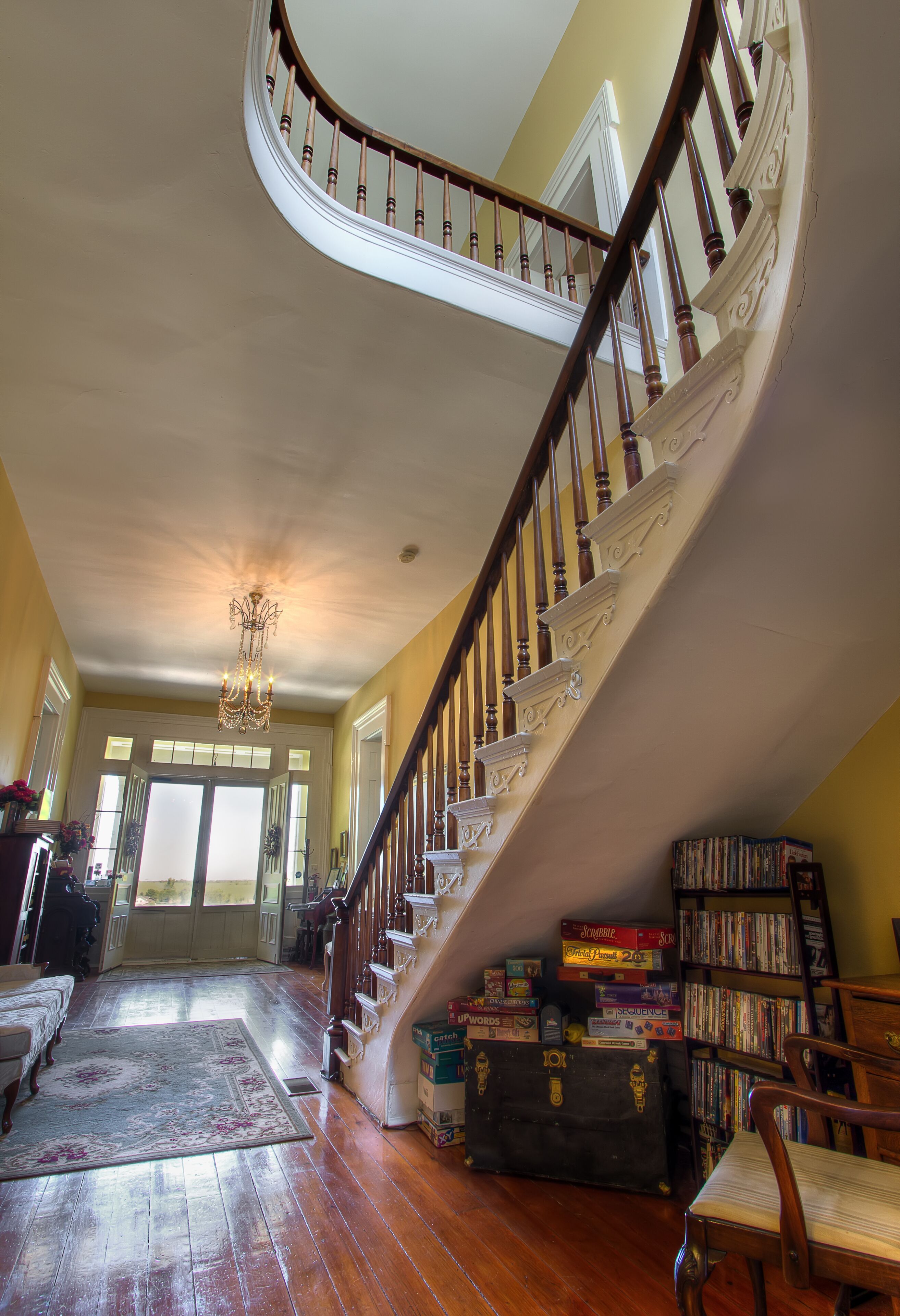 A grand staircase with a wooden handrail and white balusters, leading to a landing with a chandelier.