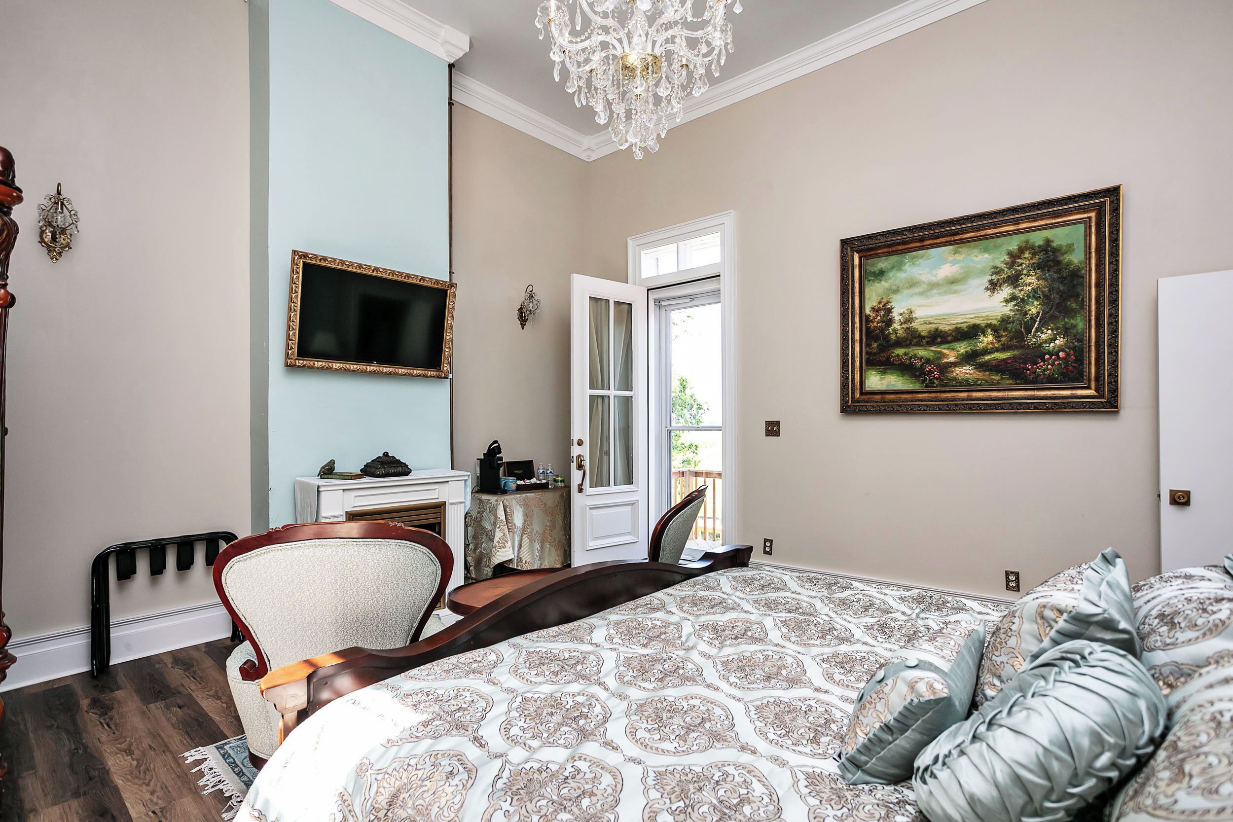 A bedroom with a large bed, a television, a painting, and a chandelier.