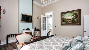 A bedroom with a large bed, a television, a painting, and a chandelier.