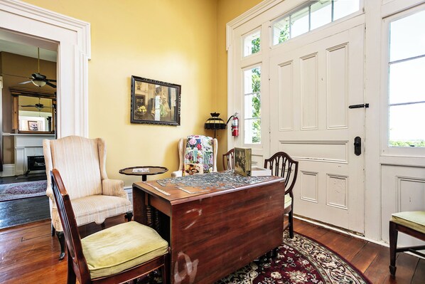A dining area with a wooden table, chairs, a floral rug, and a painting on the wall.