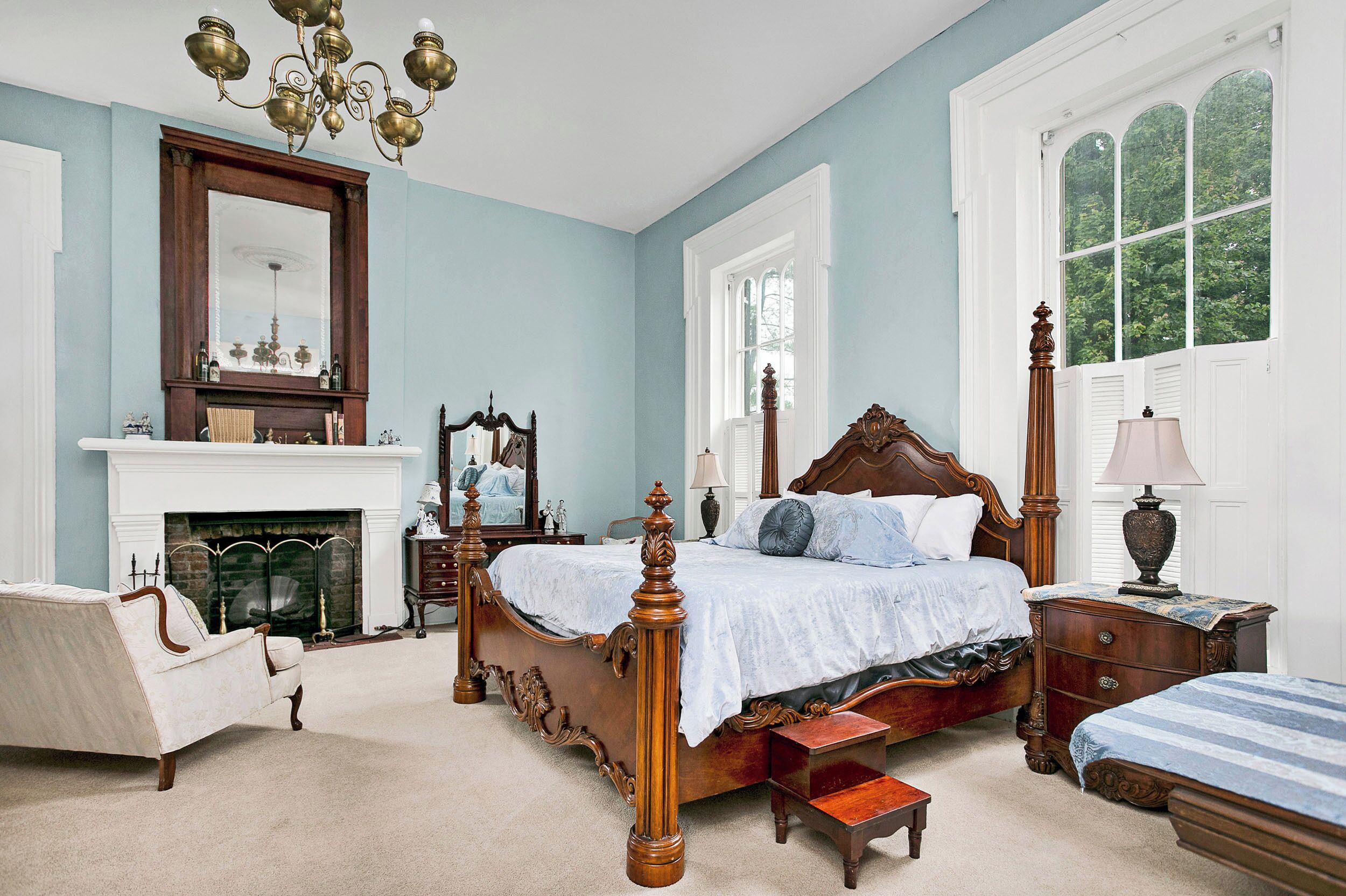 A bedroom with a large bed, a chair, a fireplace, and a window with a view of trees.