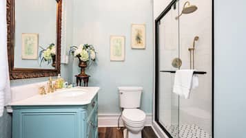 Un baño con inodoro blanco, lavabo con detalles dorados, espejo con marco decorativo y cabina de ducha con mampara de cristal.