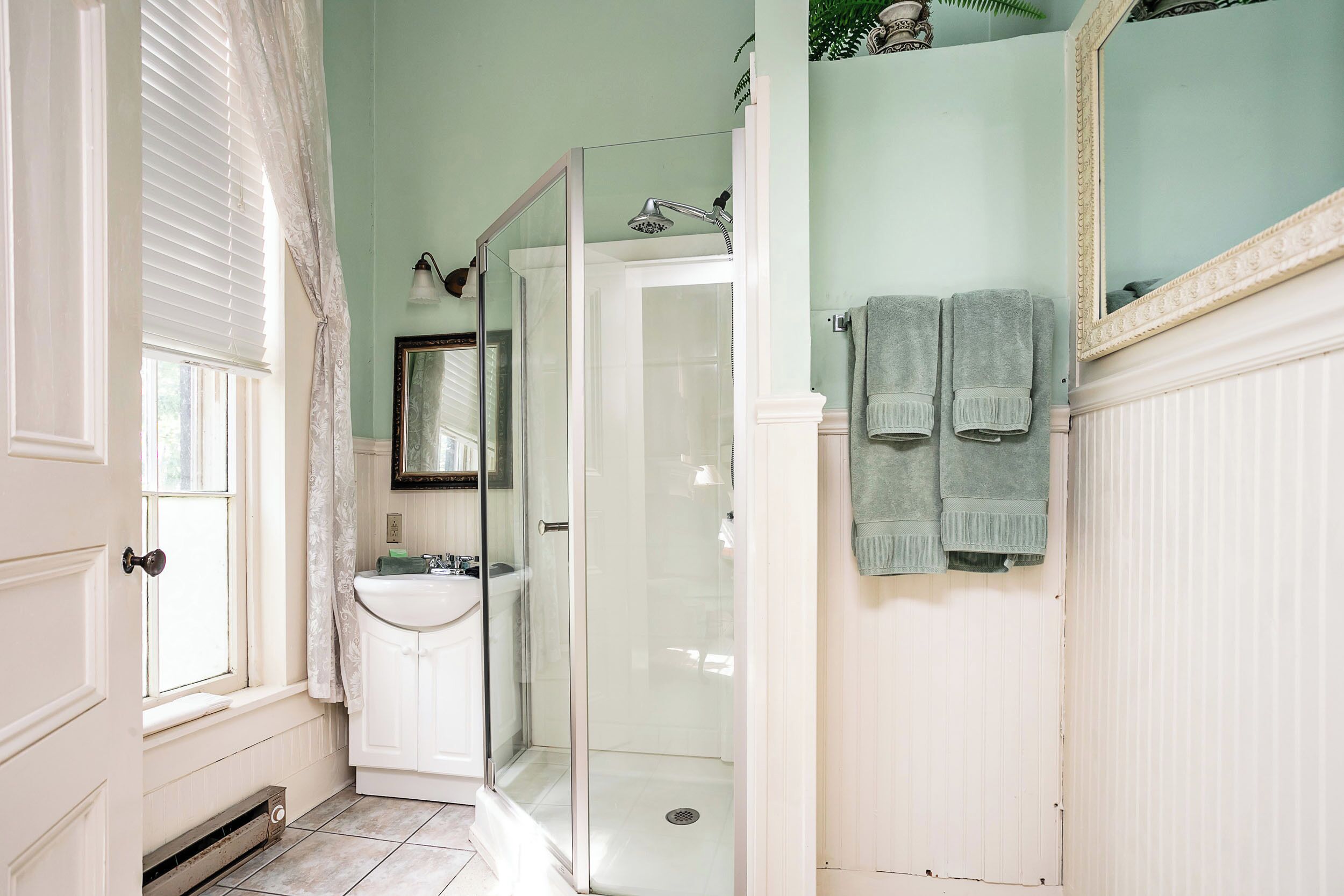 A bathroom with a glass-enclosed shower, a sink, and two towels hanging on the wall.