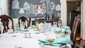 A dining table set with white and gold china, crystal glasses, and teal napkins.