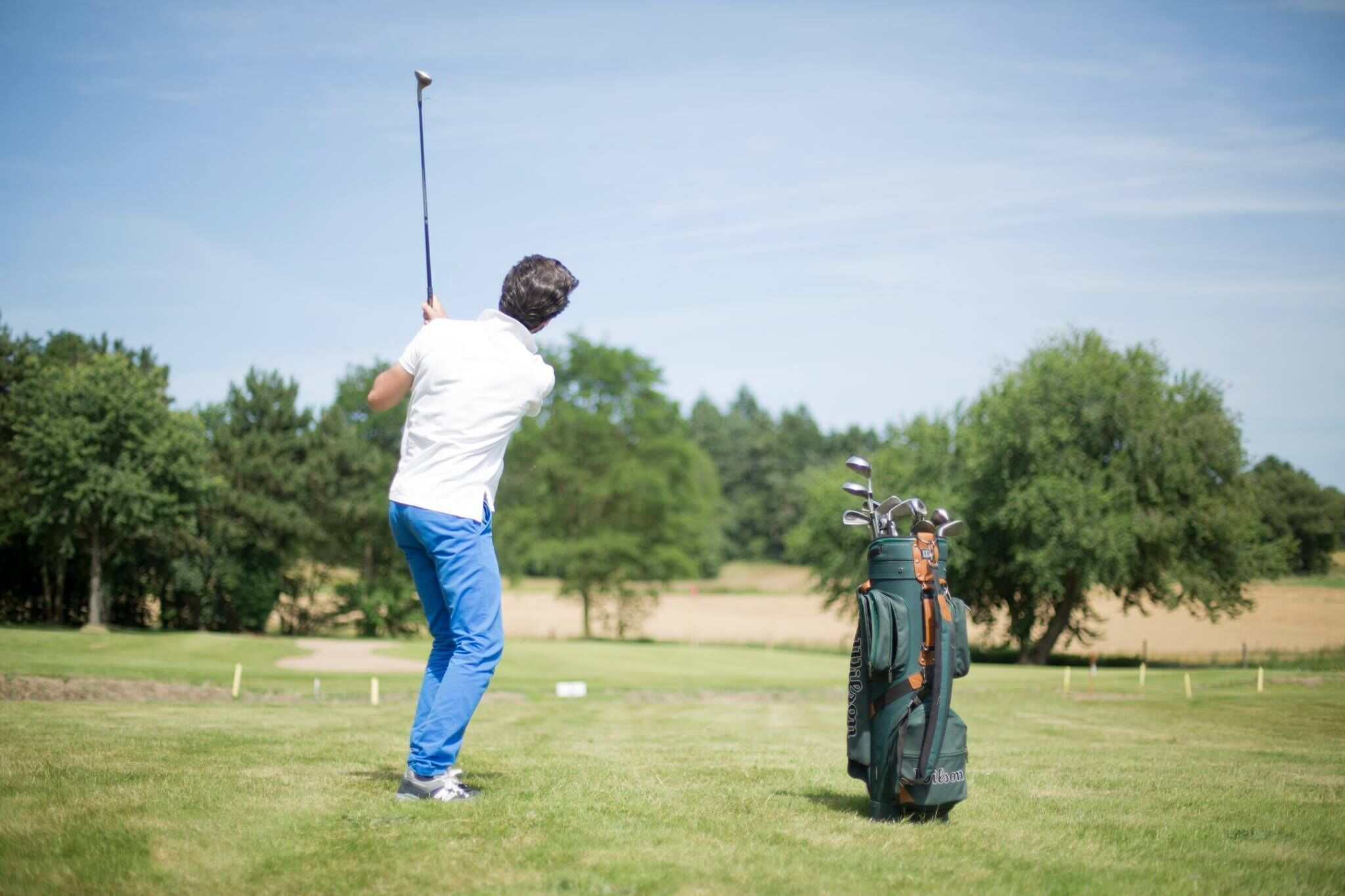 Una persona jugando golf en un campo, con un bolso de golf cerca.