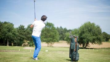 Una persona jugando golf en un campo, con un bolso de golf cerca.
