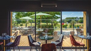 Un espacio de comedor al aire libre con mesas, sillas, sombrillas y vistas al jardín.