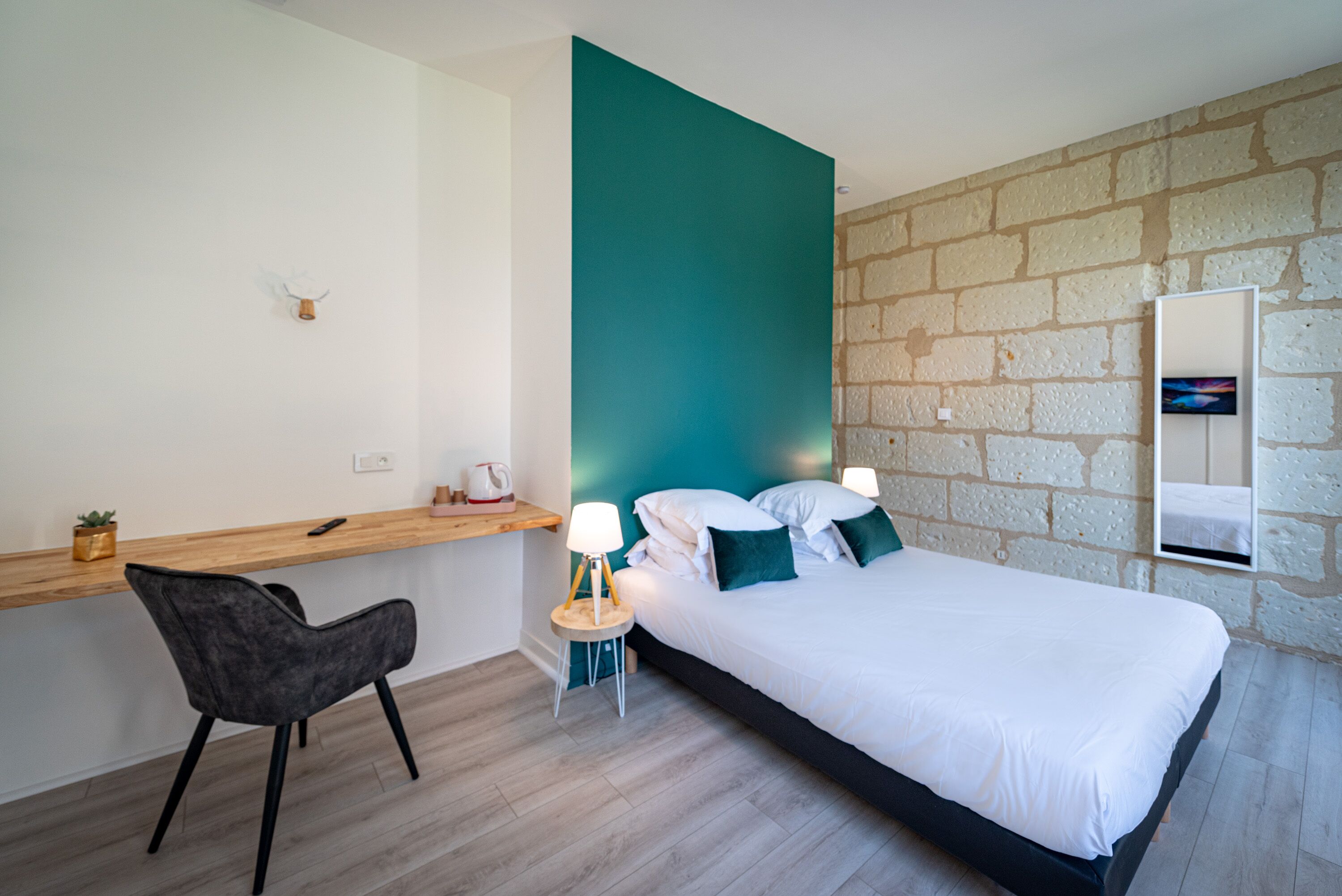 Un dormitorio moderno con cama, mesita de noche, silla y una pequeña zona de escritorio.