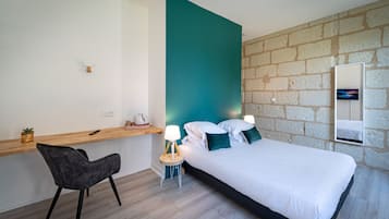 Un dormitorio moderno con cama, mesita de noche, silla y una pequeña zona de escritorio.