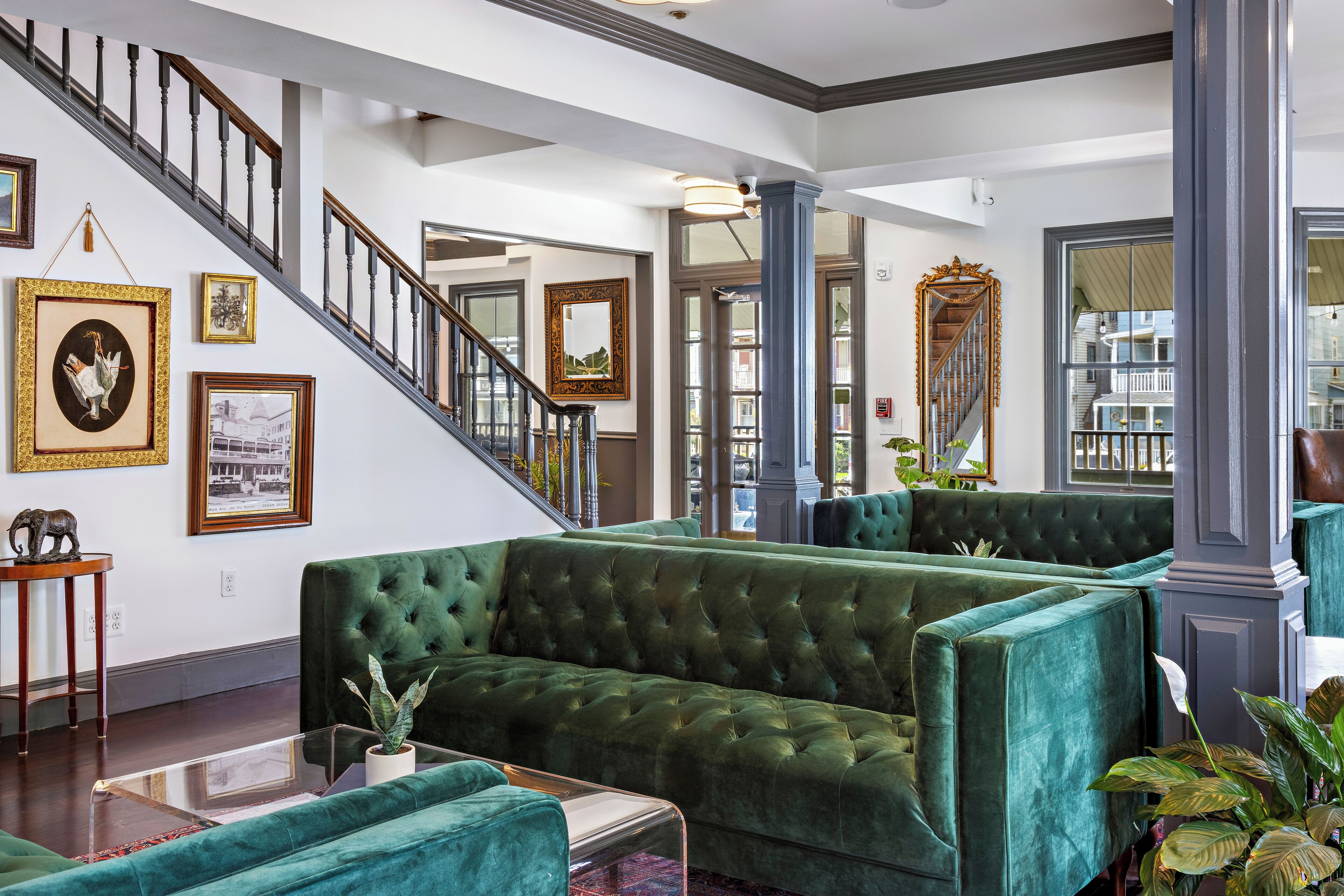 A spacious lobby with a grand staircase, green upholstered seating, and framed artwork on the walls.
