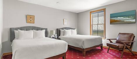 A hotel room with two beds, a red patterned carpet, a wooden chair, and a beach view through the window.