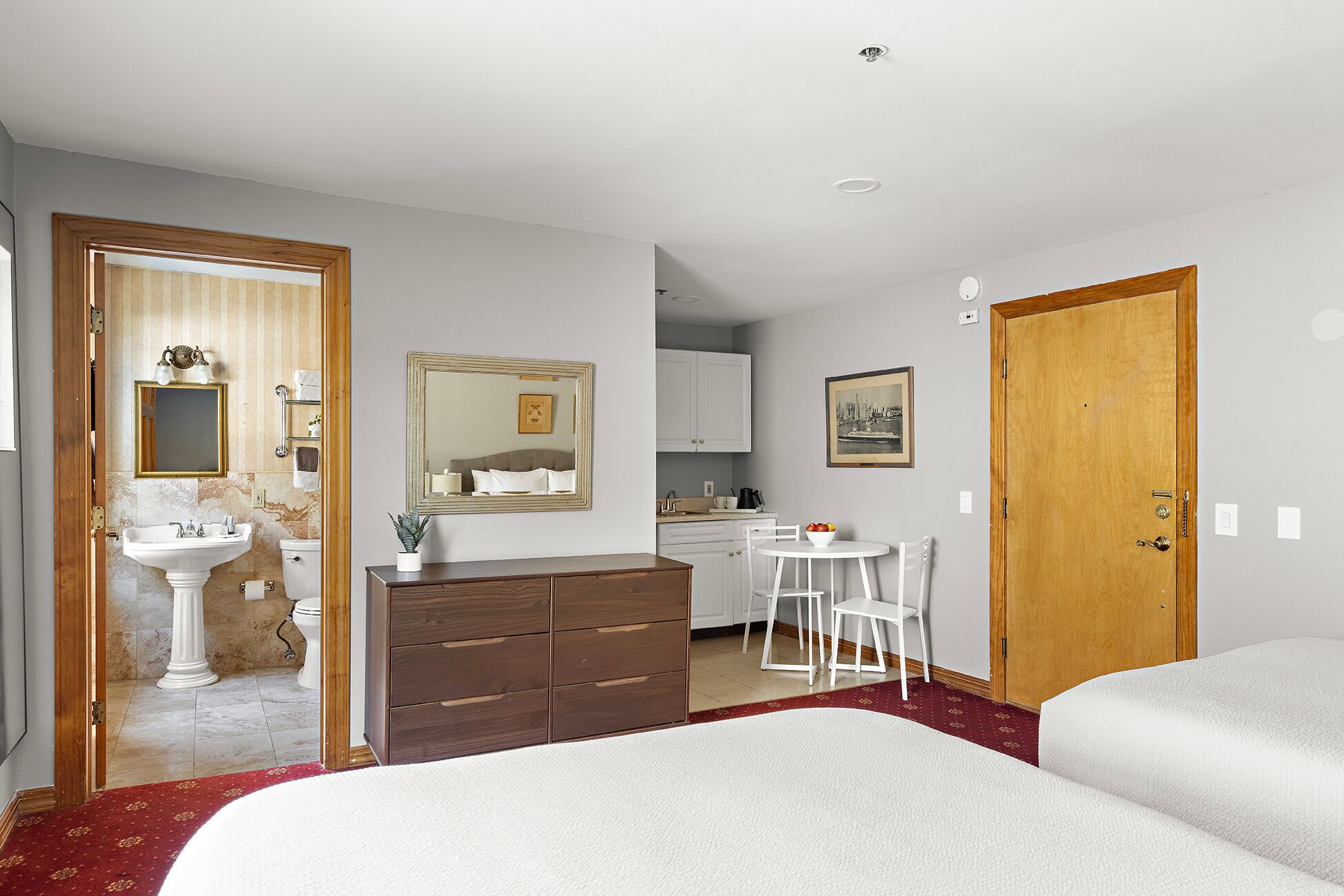 A hotel room with a bed, a desk, a chair, a sink, a mirror, a wardrobe, and a door.
