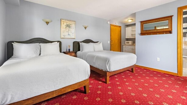 Een hotelkamer met twee bedden, een tapijtel van rood patroon, een houten deur en een kleine kitchenette op de achtergrond.