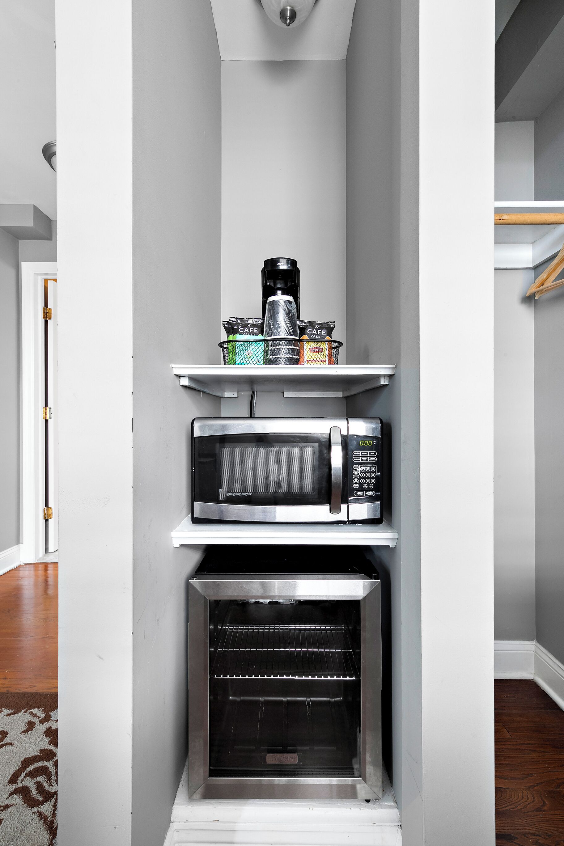 A compact kitchen with a microwave, coffee maker, and a small shelf with kitchen items.