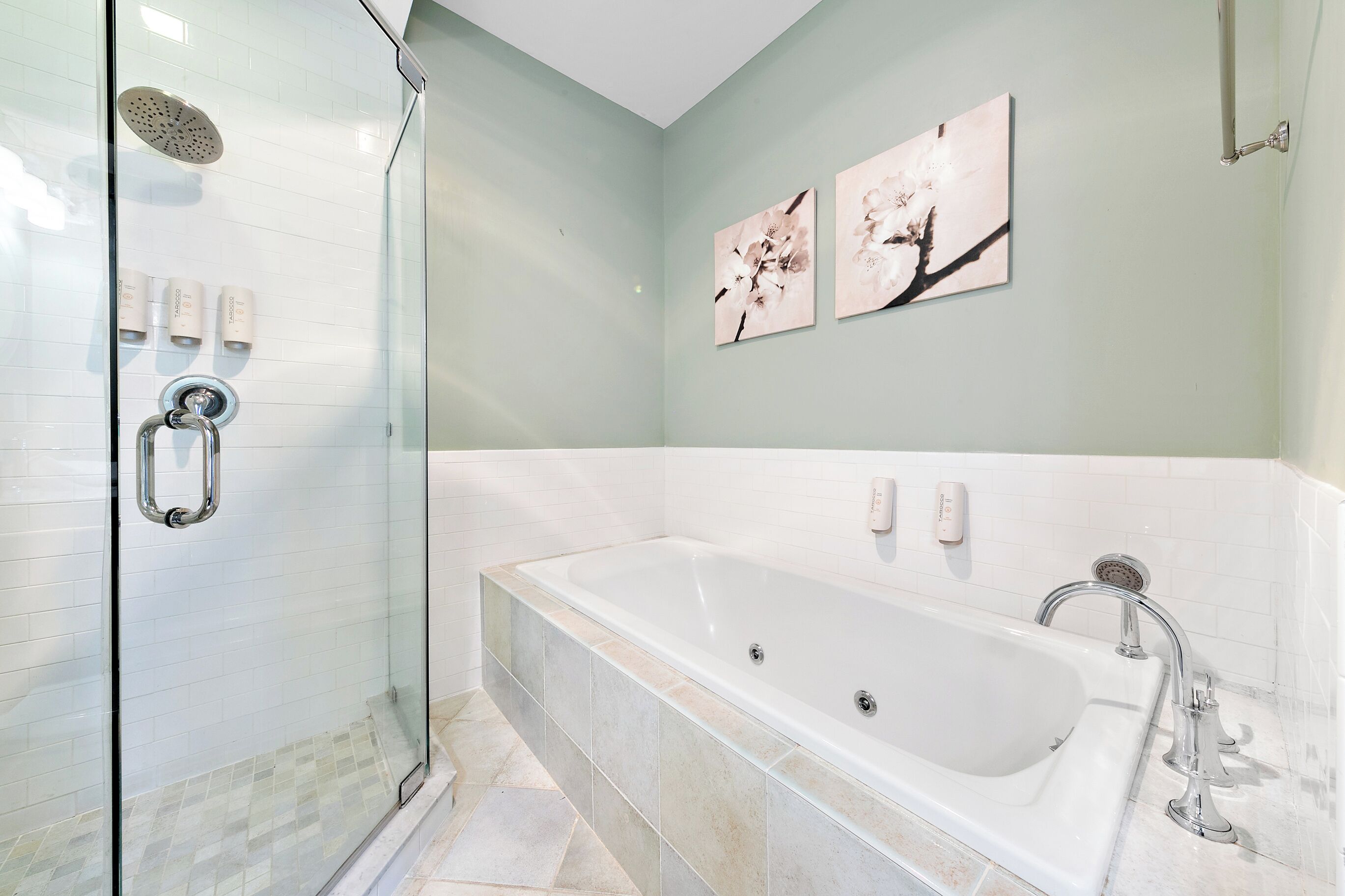 A modern bathroom with a glass-enclosed shower, a large freestanding bathtub, and two wall-mounted artwork pieces.