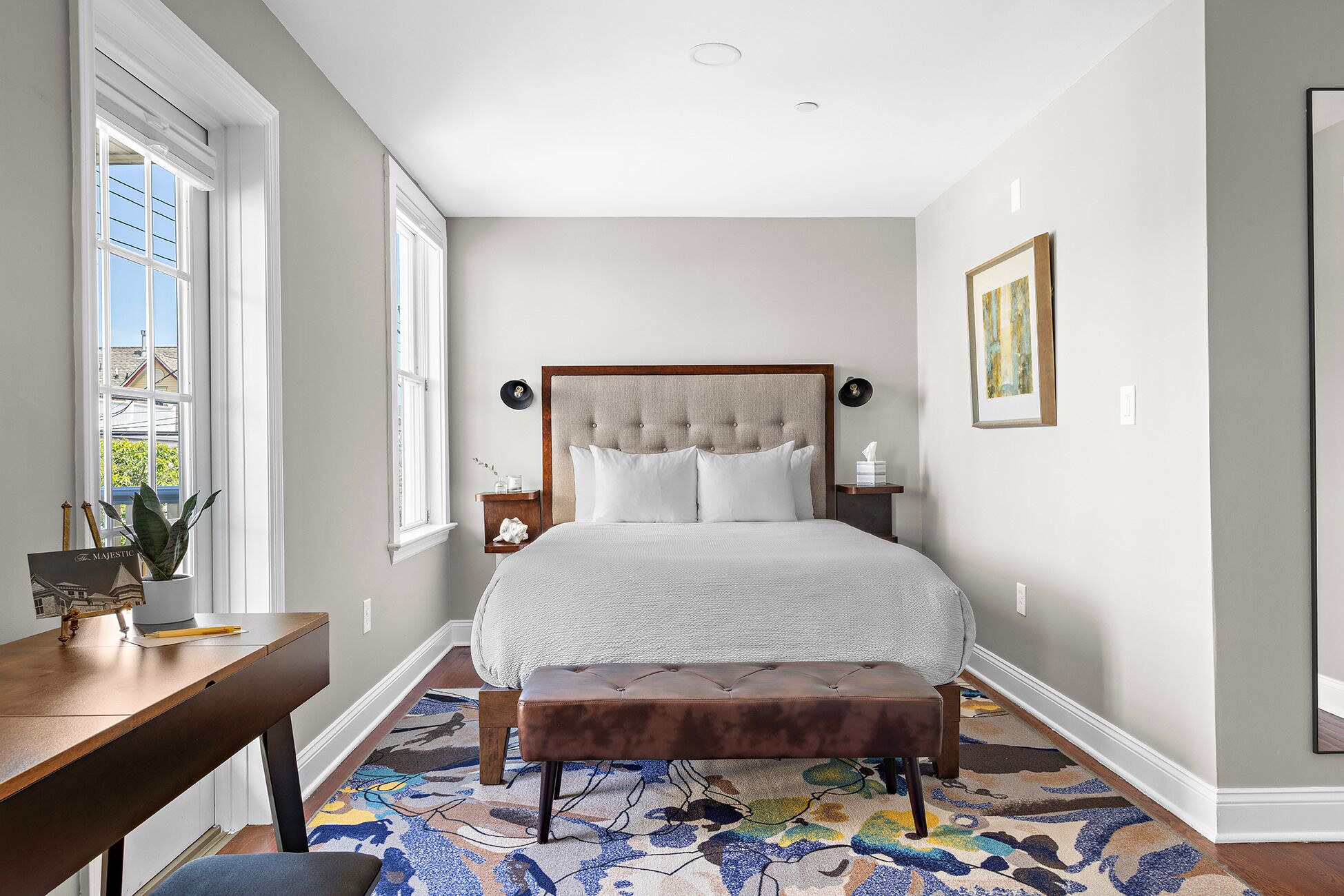 A bedroom with a large bed, a wooden desk, a bench, and a window with a view.
