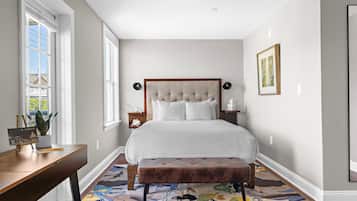 A bedroom with a large bed, a wooden desk, a bench, and a window with a view.