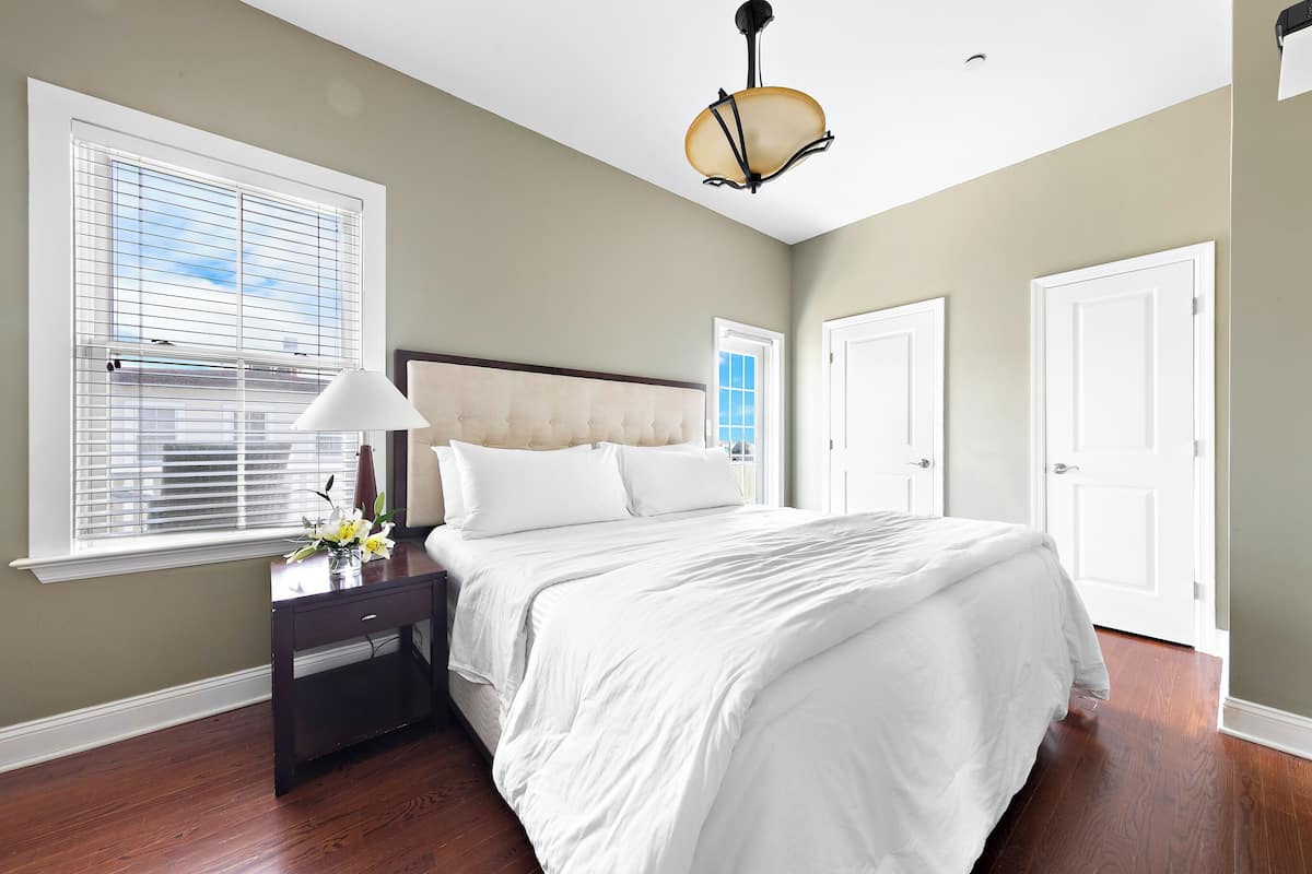 A bedroom with a large bed, a nightstand, a lamp, and a window with blinds.