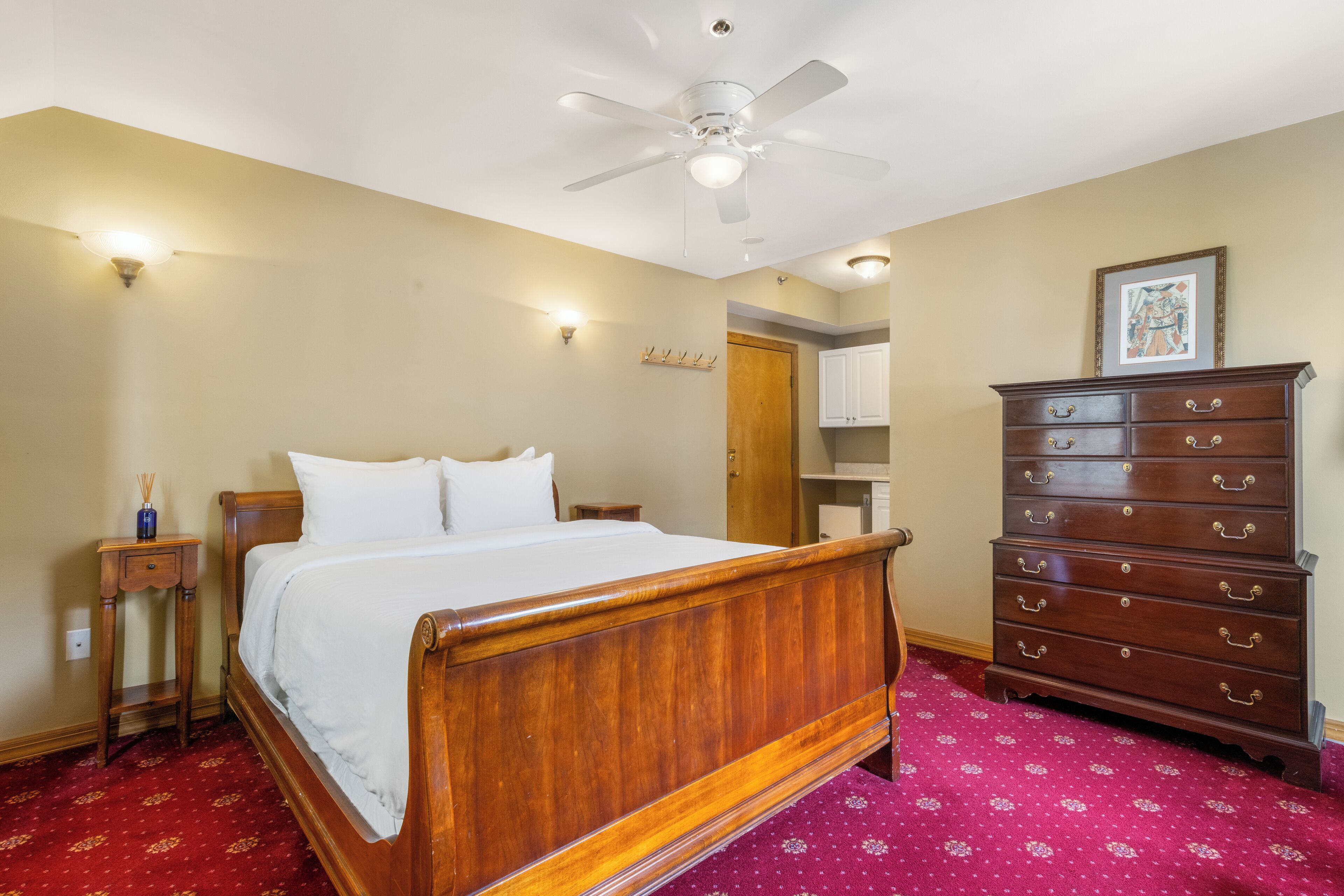 A bedroom with a wooden bed, a dresser, a ceiling fan, and a red patterned carpet.