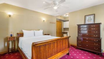 A bedroom with a wooden bed, a dresser, a ceiling fan, and a red patterned carpet.