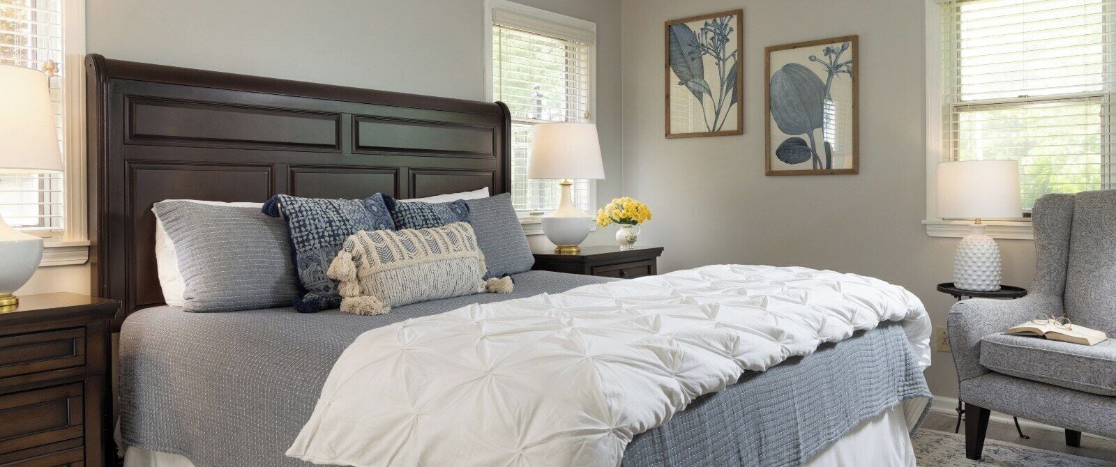 A neatly arranged bedroom with a large bed, two bedside tables, a chair, and wall art.