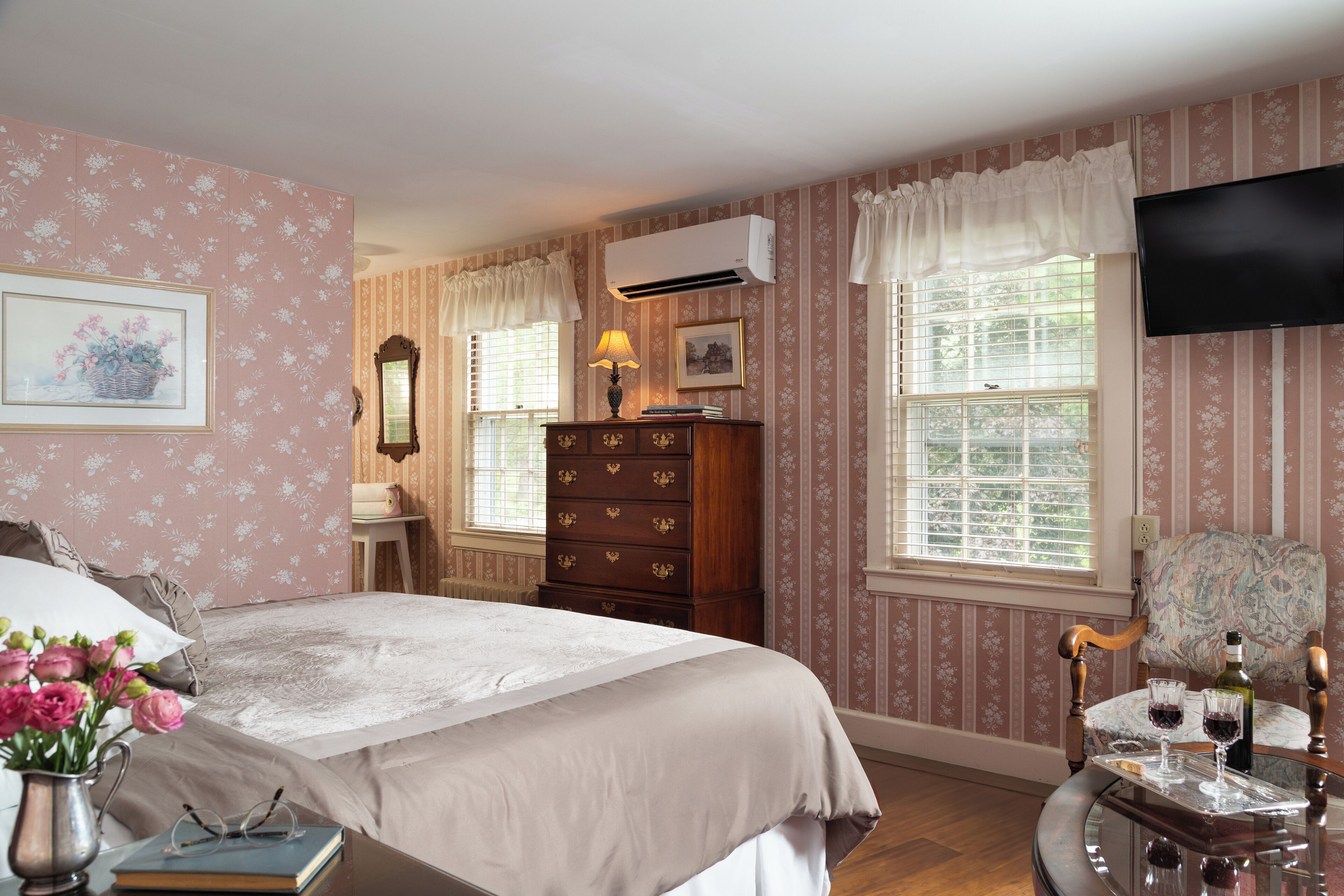 A bedroom with a bed, dresser, vanity, and a television.