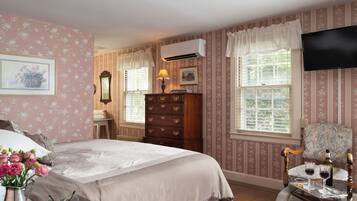 A bedroom with a bed, dresser, vanity, and a television.