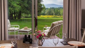 Un coin repas avec une table dressée pour deux personnes, une vue sur un paysage verdoyant à travers de grandes fenêtres et des sièges extérieurs offrant également une vue.