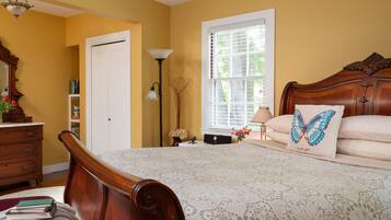 A bedroom with a wooden bed, a nightstand, a dresser, a lamp, and a window with blinds.