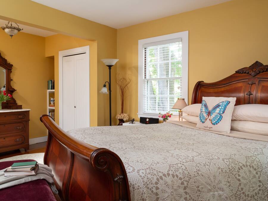 A bedroom with a wooden bed, a nightstand, a dresser, a lamp, and a window with blinds.